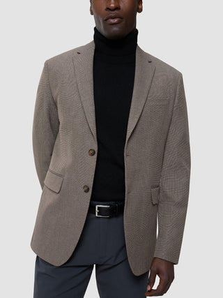 Ein Mann, der einen hellbraunen „Essential Blazer“ über einem schwarzen „Cooler than classic“-Shirt trägt.