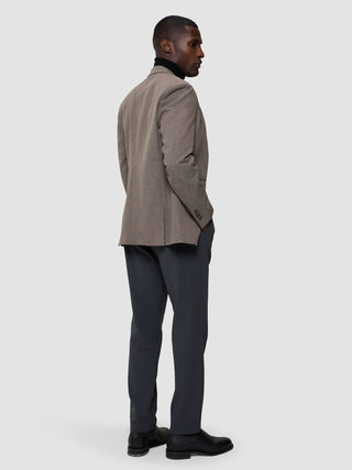 Ein Mann, der einen schwarzen „Cooler than classic“-Pullover über einem schwarzen Rollkragenpullover aus Merinowollmischung trägt, dazu eine dunkle Hose und schwarze Anzugschuhe, steht mit dem Rücken zur Kamera.