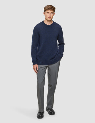 Ein Mann, der einen dunkelblauen, melierten Pullover aus weicher, dicker Wolle mit Rundhalsausschnitt, eine graue Hose und schwarze Lederschuhe trägt.