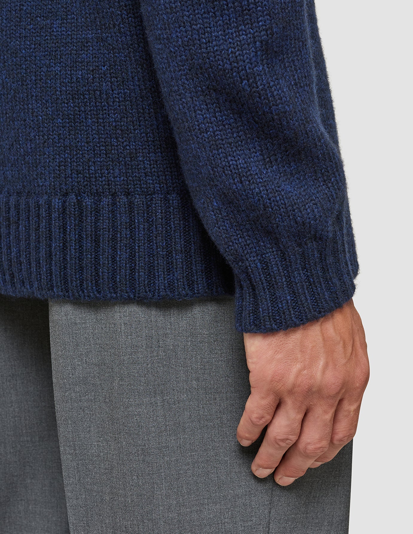 Nahaufnahme einer Person, die einen dunkelblauen, melierten Chunky Soft Wool Knit Crewneck trägt – einen Pullover aus grober, weicher Wolle mit geripptem Saum und Bündchen –, kombiniert mit einer grauen Hose.