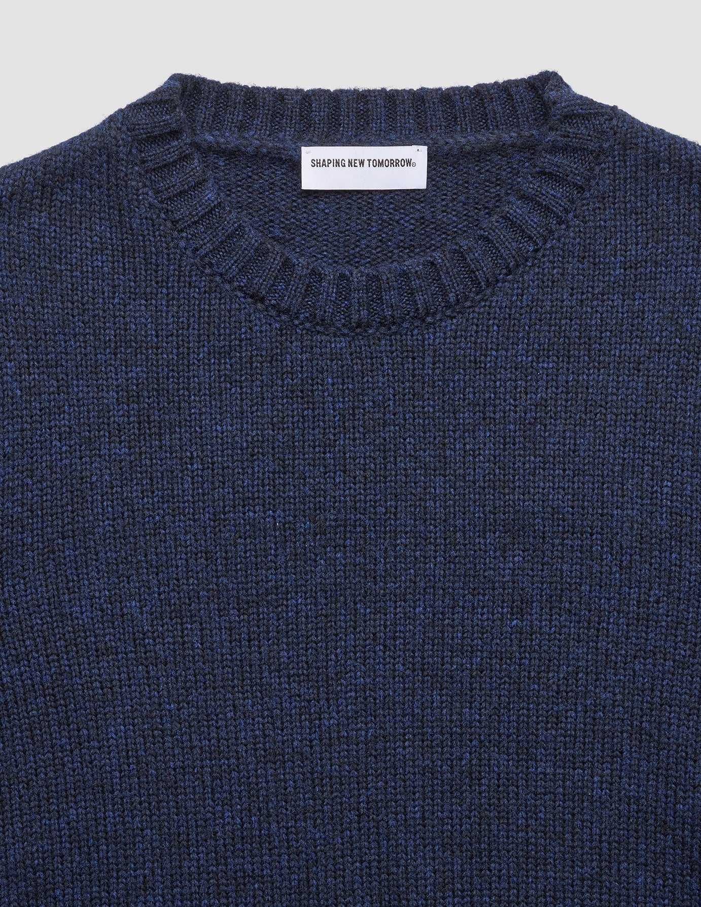 Dicker, weicher Wollpullover mit Rundhalsausschnitt in dunklem Marineblau-Melange, der sich durch eine grobe Strickstruktur und ein sichtbares Markenetikett an der Innenseite des Halsausschnitts auszeichnet.