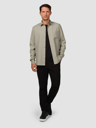 Ein Mann, der ein „Effortless Shirt“ in der Farbe „Stone Beige“ über einem schwarzen T-Shirt, einer schwarzen Hose und schwarzen Sneakern trägt.