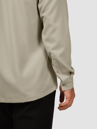 Nahaufnahme des Rückens und des Ärmels eines „Effortless Shirt Stone Beige“ aus recyceltem Polyester, kombiniert mit einer schwarzen Hose.