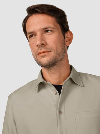 Ein Mann blickt zur Seite; er trägt ein „Effortless“-Hemd in der Farbe „Stone Beige“ über einem schwarzen T-Shirt.