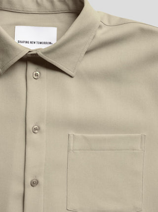 „Effortless Shirt“ – ein beiges Button-Down-Hemd in der Farbe „Stone Beige“ mit einer Brusttasche und einem „Shaping New Tomorrow“-Markenlabel auf der Innenseite des Kragens.