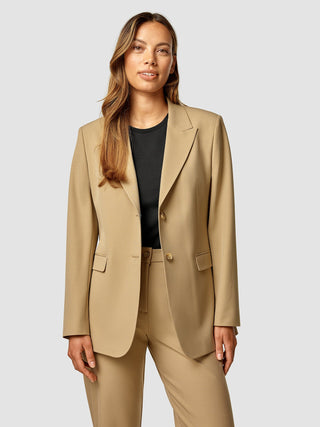 Eine Frau, die einen hellbraunen „Essential Blazer Caramel“ über einem schwarzen Oberteil trägt.