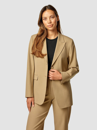 Eine Frau, die einen hellbraunen „Essential Blazer Caramel“ über einem schwarzen Oberteil trägt.