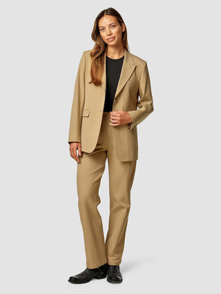 Eine Frau, die einen „Essential Blazer“ in der Farbe „Caramel“ und eine dazu passende Hose über einem schwarzen Hemd trägt.