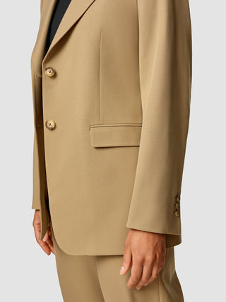 Eine Person, die einen hellbraunen „Essential Blazer Caramel“ trägt.