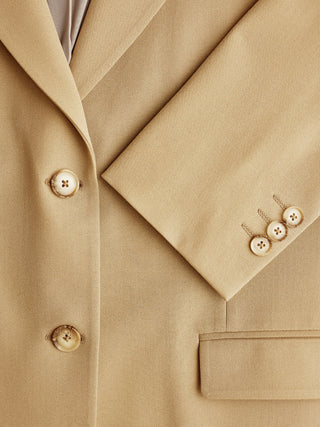 Eine Nahaufnahme eines hellbraunen „Essential Blazer Caramel“, auf der das Revers, die Knöpfe auf der Vorderseite und die Knöpfe an den Ärmelbündchen zu sehen sind.
