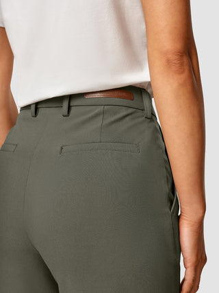 Eine Person, die ein weißes T-Shirt trägt, das in eine „Essential Pants Straight Dark Olive“ mit einem Marken-Lederpatch am Bund gesteckt ist.