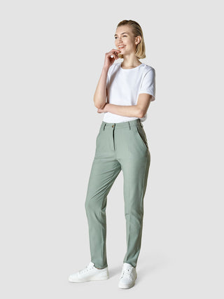 Eine lächelnde Frau, die ein weißes T-Shirt, eine „Essential Pants Tapered“ in der Farbe „Calm Green Melange“ und weiße Sneaker trägt – ein Look im skandinavischen Design.