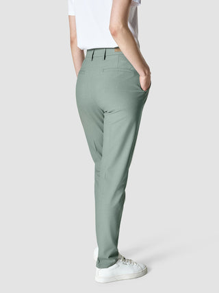 Eine Person, die ein weißes T-Shirt und eine „Essential Pants Tapered Calm Green Melange“ trägt und die Hände in den Taschen hat.