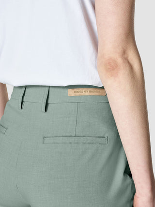 Nahaufnahme der Hose „Essential Pants Tapered Calm Green Melange“ mit einem Lederetikett mit der Aufschrift „SHAPING NEW TOMORROW“ am hinteren Bund.