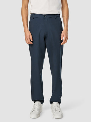 Eine Person, die ein weißes T-Shirt, eine „Essential Pants Relaxed Fit Navy Melange“ und weiße Sneaker trägt.