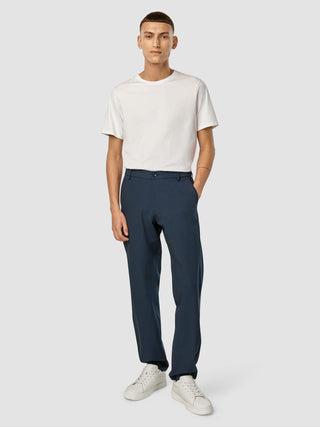 Ein Mann, der ein weißes T-Shirt, eine „Essential Pants Relaxed Fit Navy Melange“ und weiße Sneaker trägt.