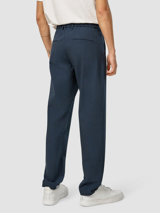 Rückansicht einer Person, die eine marineblaue „Essential Pants Relaxed Fit Navy Melange“ und weiße Sneaker trägt.