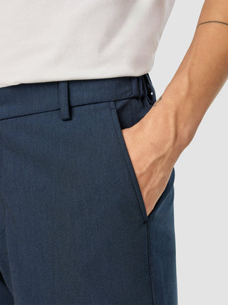 Eine Person, die eine „Essential Pants Relaxed Fit Navy Melange“ trägt und eine Hand in der Hosentasche hat.