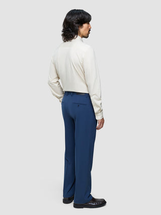 Ein Mann, von hinten gesehen, der ein cremefarbenes Langarmhemd und eine „Essential Suit Pants Relaxed Fit“ in Marineblau trägt.
