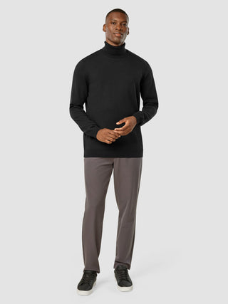 Ein Mann, der einen schwarzen „Everyday Knit“-Rollkragenpullover, eine dunkelgraue Hose und schwarze Sneaker trägt.