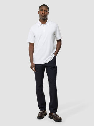 Ein Mann, der ein weißes „Evolve Pique Polo“, eine dunkle Hose und braune Slipper trägt – ein Must-have für den Sommer.