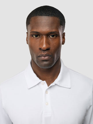 Ein Mann mit ernstem Gesichtsausdruck, der ein weißes „Evolve Pique Polo“ trägt – ein Sommer-Must-have im skandinavischen Design.