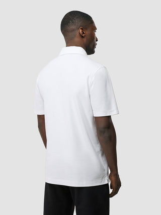Ein Mann, von hinten gesehen, der ein weißes „Evolve Pique Polo“ und schwarze Shorts trägt und damit das skandinavische Design verkörpert.
