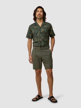 Ein Mann, der ein grünes Hemd mit botanischem Muster und kurzen Ärmeln, GEN2™-Shorts in „Muted Green“ und schwarze Sandalen trägt.