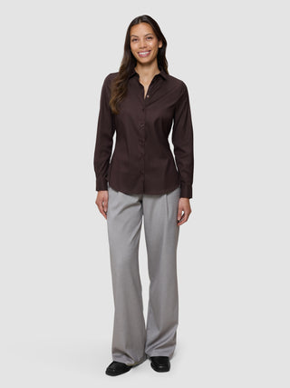 Eine lächelnde Frau, die ein Damen-Oxfordhemd in der Farbe „Espresso“ in regulärer Passform und eine graue Hose trägt und damit ein Beispiel für skandinavisches Design präsentiert.