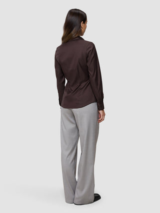 Eine Person, von hinten gesehen, die ein Damen-Oxfordhemd in der Farbe „Espresso Regular“ trägt, das in eine hellgraue Hose gesteckt ist – ein Look, der vom skandinavischen Design geprägt ist.