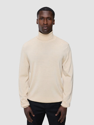 Ein Mann, der einen nahtlosen Premium-Merino-Strickpullover mit Rollkragen in der Farbe „Birchwood“ trägt.