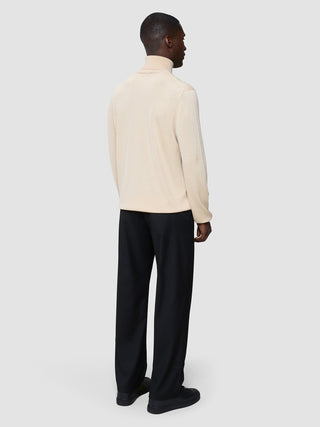 Ein Mann, von hinten gesehen, der einen nahtlosen Premium-Merinostrick-Rollkragenpullover „Birchwood“, eine schwarze Hose und schwarze Sneaker trägt.
