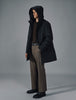 Ein Mann, der eine schwarze Utility-Jacke, einen dunkelbraunen Pullover, eine braune Hose und schwarze Schuhe trägt.