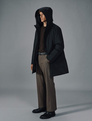 Ein Mann, der eine schwarze Utility-Jacke, einen dunkelbraunen Pullover, eine braune Hose und schwarze Schuhe trägt.