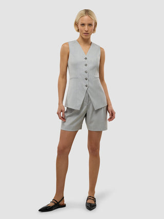 Eine Frau trägt ein hellgraues „Skye Set Grey Pine Melange“ aus langer Weste und Shorts, das sich durch eine schlichte, skandinavische Ästhetik auszeichnet.