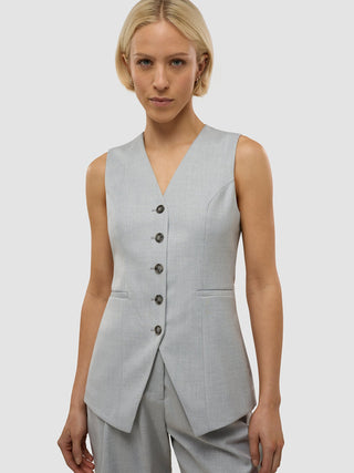 Eine Frau, die das „Skye Set Grey Pine Melange Long Vest & Shorts“ trägt, eine taillierte, hellgraue, ärmellose Weste mit Knopfleiste, die sich durch eine schlichte, skandinavische Ästhetik auszeichnet.