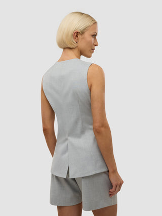 Eine Frau, von hinten gesehen, die ein hellgraues „Skye Set Grey Pine Melange“ aus langer Weste und Shorts trägt, das sich durch ein minimalistisches skandinavisches Design auszeichnet.