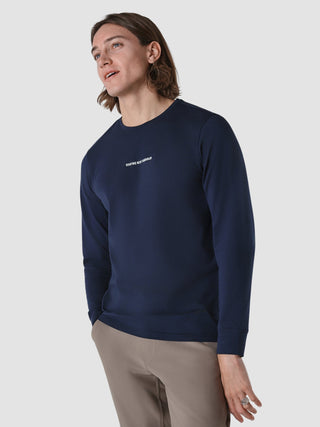 Ein Mann, der ein langärmeliges „Supima Autograph“-T-Shirt in Marineblau trägt, auf dessen Brust der Schriftzug „SHAPING NEW TOMORROW“ aufgedruckt ist.