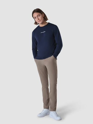Eine Person, die ein langärmeliges „Supima Autograph“-T-Shirt in Marineblau, eine hellbraune Hose und weiße Sneaker trägt.