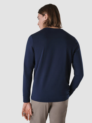 Rückansicht einer Person, die ein langärmeliges „Supima Autograph“-T-Shirt in Marineblau und eine hellbraune Hose im schlichten, skandinavischen Design trägt.
