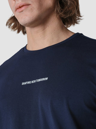 Eine Person, die ein langärmeliges Supima Autograph-T-Shirt in Marineblau trägt, auf dessen Brust in minimalistischem, skandinavischem Design der Schriftzug „SHAPING NEW TOMORROW“ aufgedruckt ist.