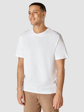 Ein Mann, der ein weißes „Supima T-Shirt Box Fit Legacy“ mit einem kleinen gestickten Logo auf der Brust trägt, das sich durch ein schlichtes, skandinavisches Design auszeichnet.