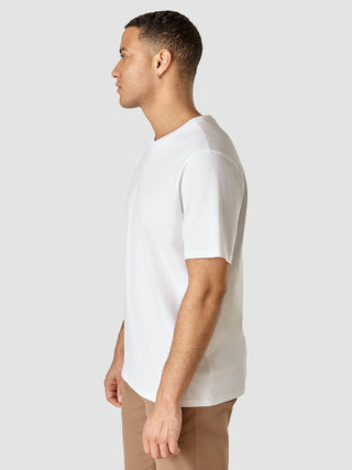 Ein Mann im Profil, der ein Supima-T-Shirt in der Passform „Box Fit Legacy“ in Weiß und eine hellbraune Hose mit 360°-Stretch trägt.