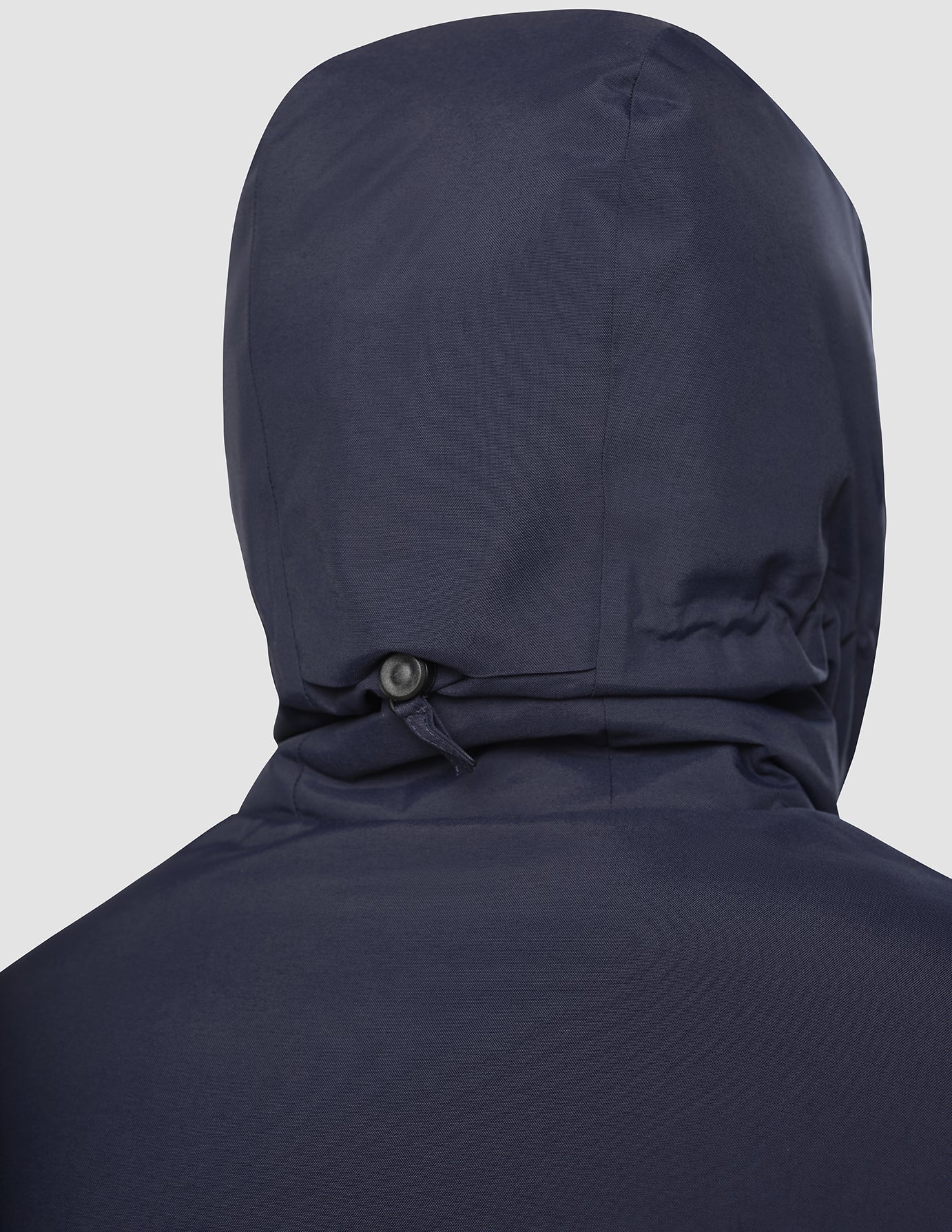 Eine Person, die eine dunkelblaue Utility-Jacke mit Kapuze und einem verstellbaren Kordelzug mit Stopper im Nacken trägt.