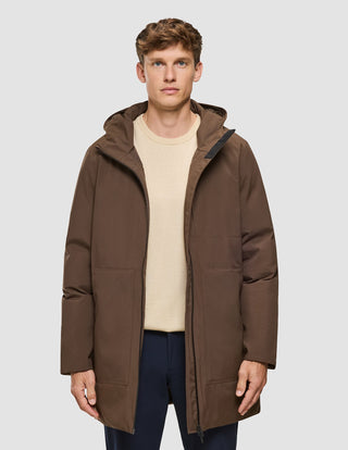 Ein Mann, der eine sattelbraune Utility-Jacke – ein mittellanges, winddichtes Modell mit Kapuze – über einem beigen Pullover trägt.