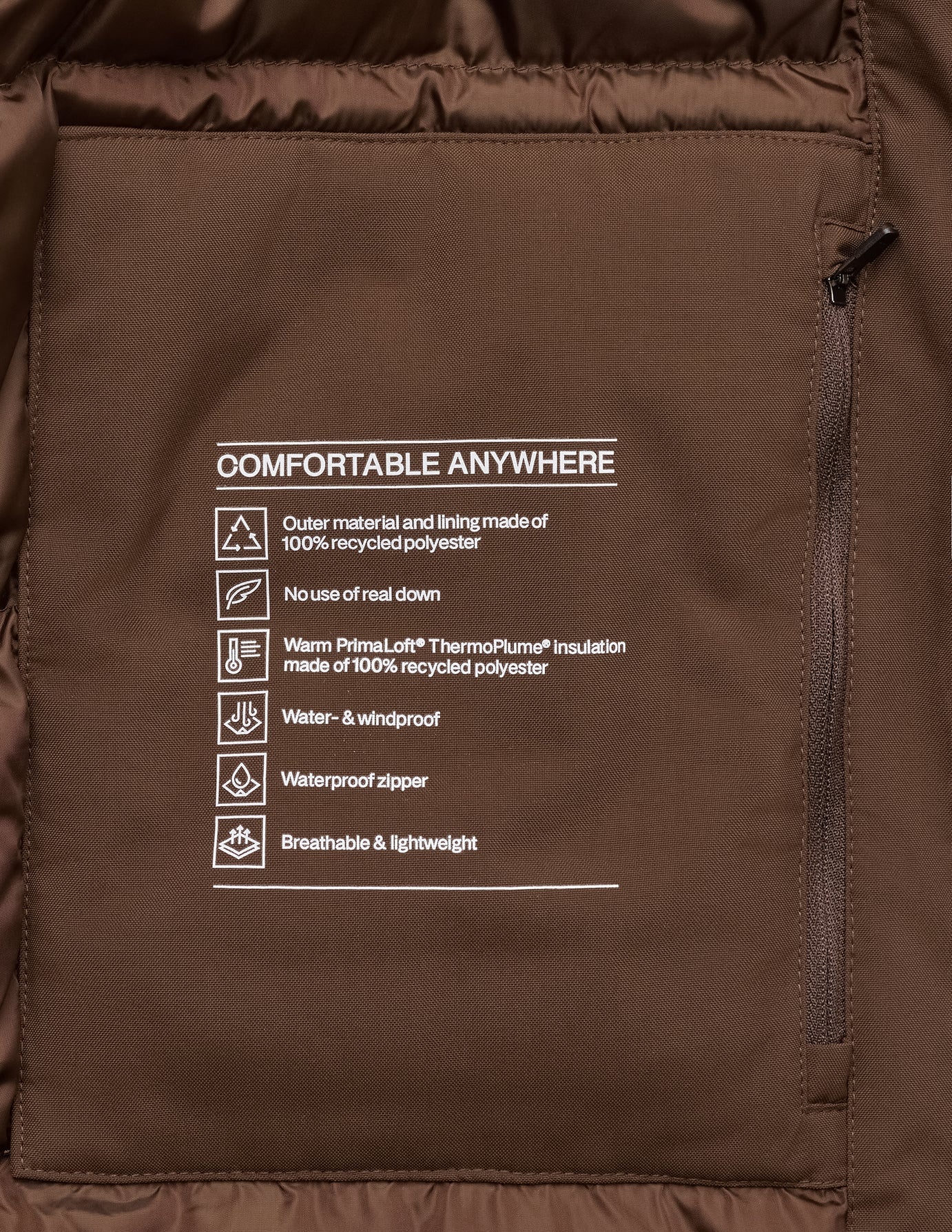 Innentasche einer sattelbraunen Utility-Jacke mit einem Comfortable Anywhere-Etikett, auf dem recyceltes Polyester, synthetische Isolierung und wasserabweisende Eigenschaften aufgeführt sind.
