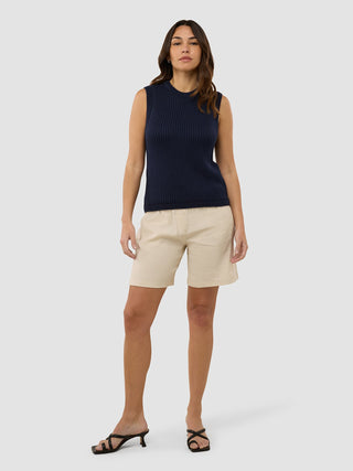 Eine Frau, die ein marineblaues, strukturiertes Strickoberteil für Damen mit beigen Shorts und schwarzen Riemchensandalen trägt.