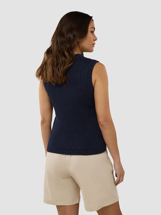Eine Frau, die ein strukturiertes Strickoberteil für Damen in Marineblau und beigefarbene Shorts im schlichten, skandinavischen Design trägt.