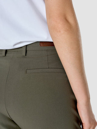 Eine Seitenansicht einer Person, die eine Hose aus der „Essential Suit Straight Dark Olive“-Kollektion trägt, mit einem kleinen braunen Lederetikett mit dem Markenlogo auf der Rückseite des Hosenbunds.