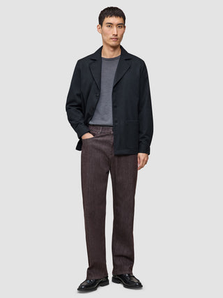 Ein Mann, der ein Atelier Overshirt Dark Navy über einem grauen T-Shirt, eine braune Atelier-Hose und schwarze Lederschuhe trägt.